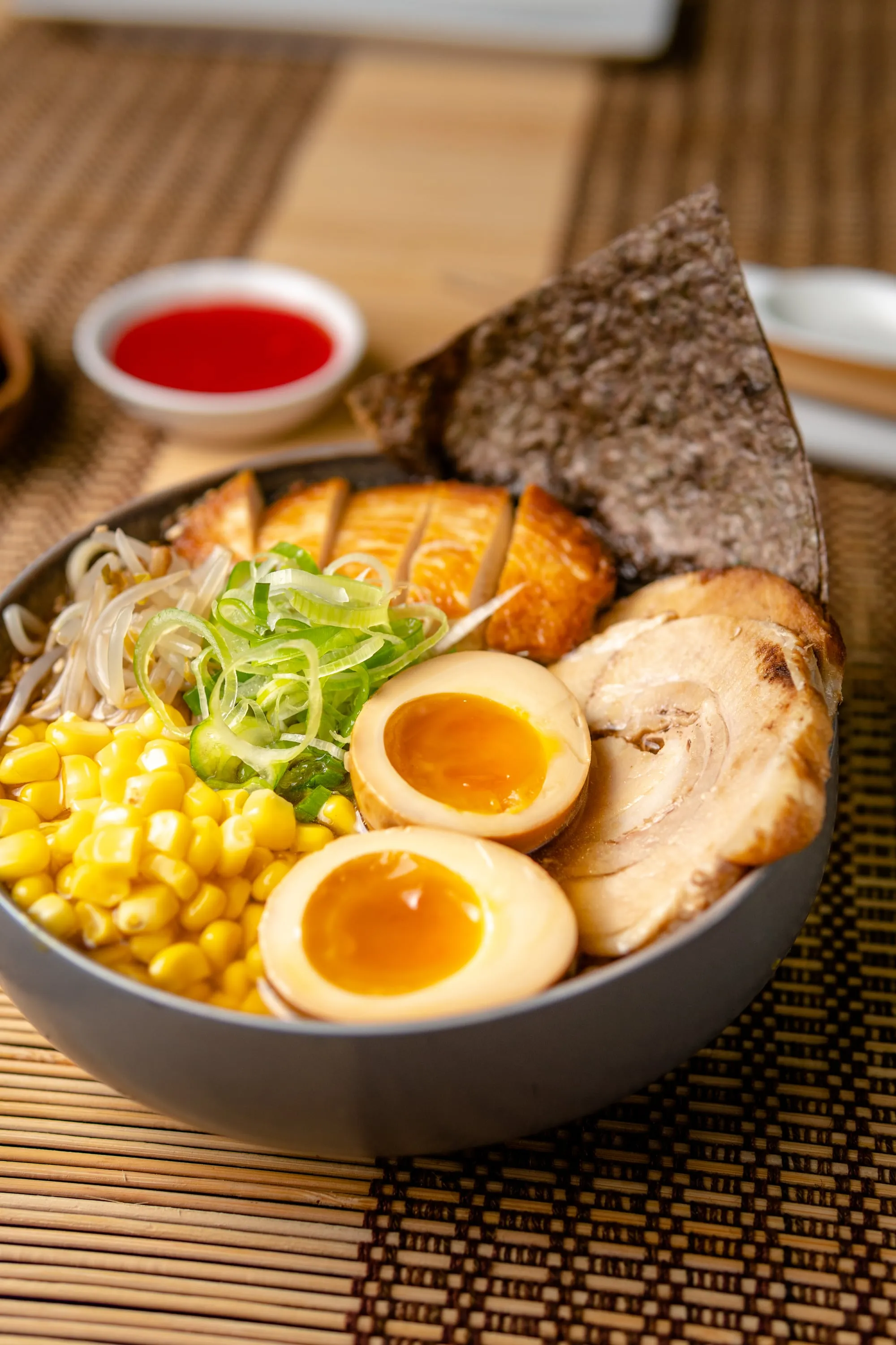 Bowl de ramen con huevos marinados, choclo, cerdo, brotes y alga nori sobre un individual de bambú