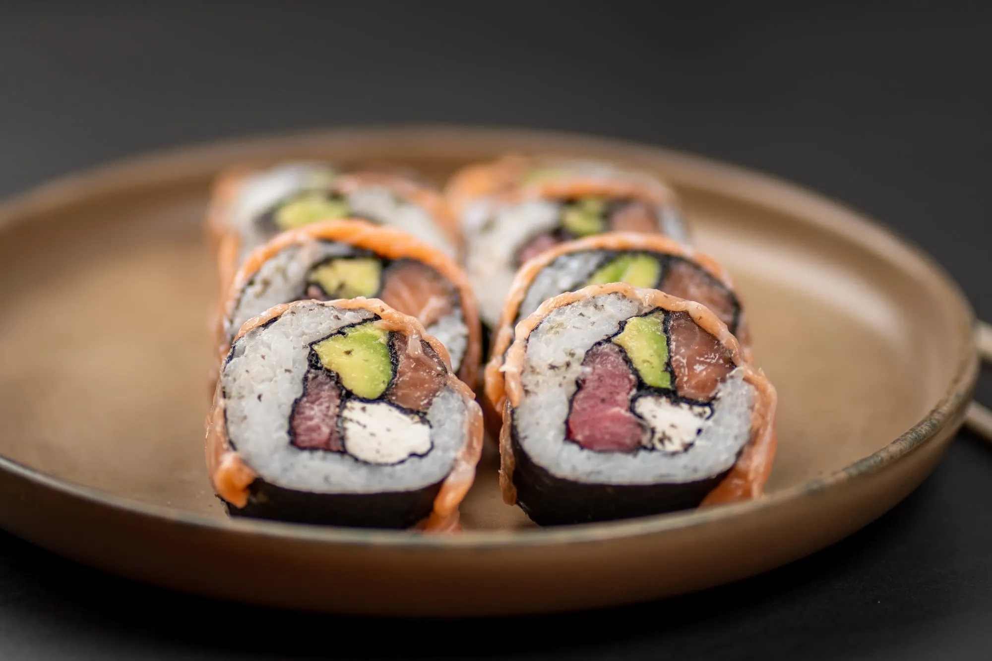 Rolls de sushi envueltos en salmón, con palta, atún y queso crema, sobre un plato de cerámica