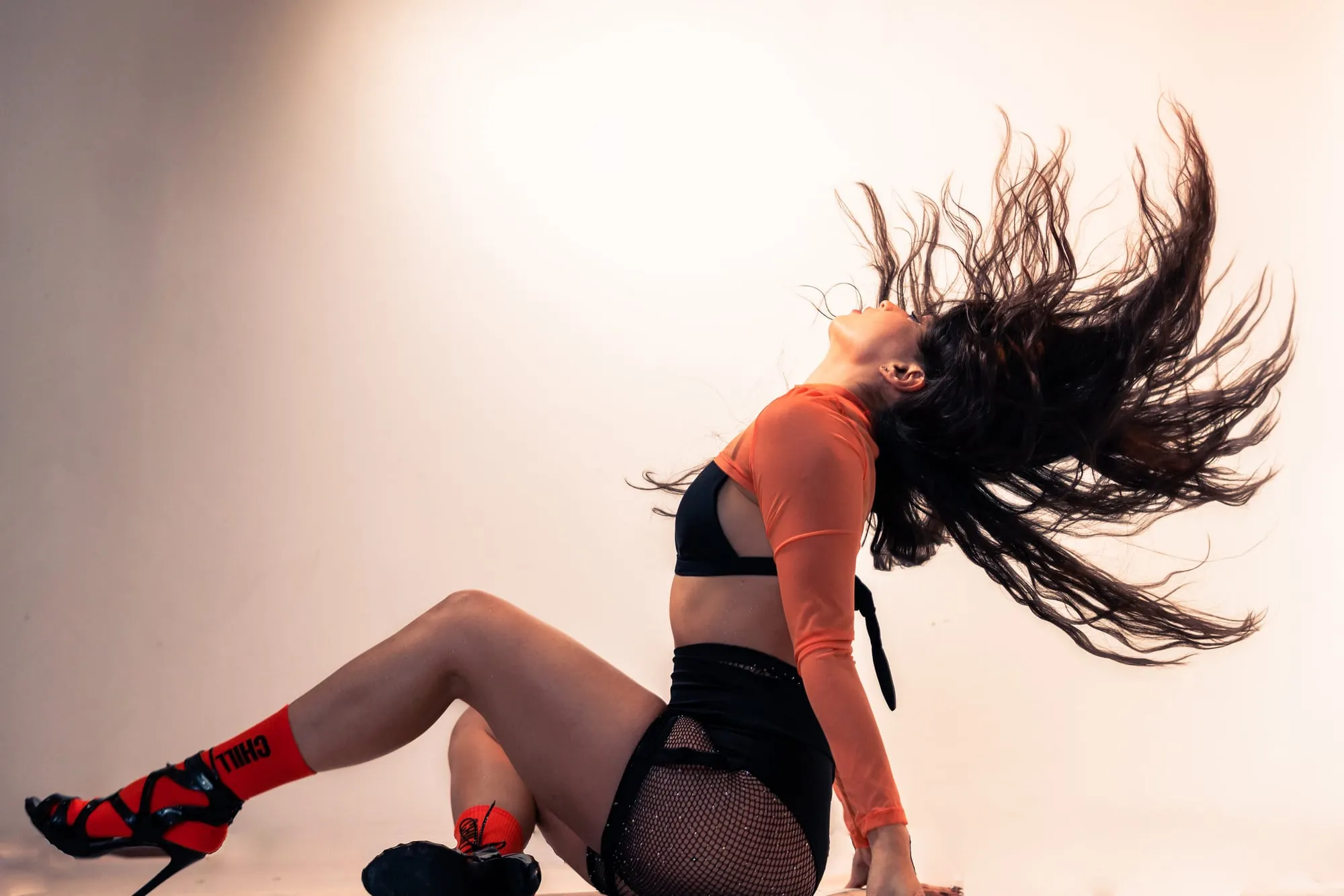Mujer sentada en el piso lanza el pelo hacia atrás en pleno movimiento, sobre un fondo claro de estudio