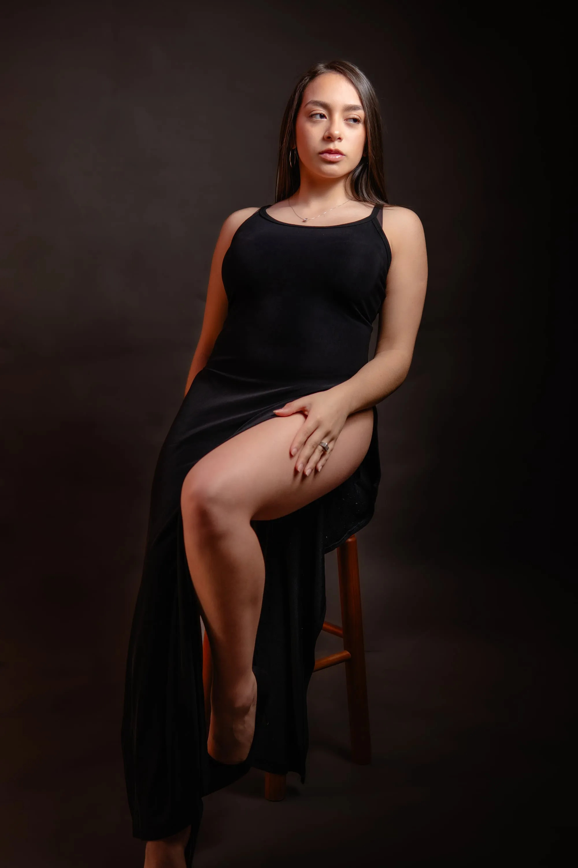 Mujer con vestido negro largo sentada en un taburete, en un retrato de estudio de luz suave